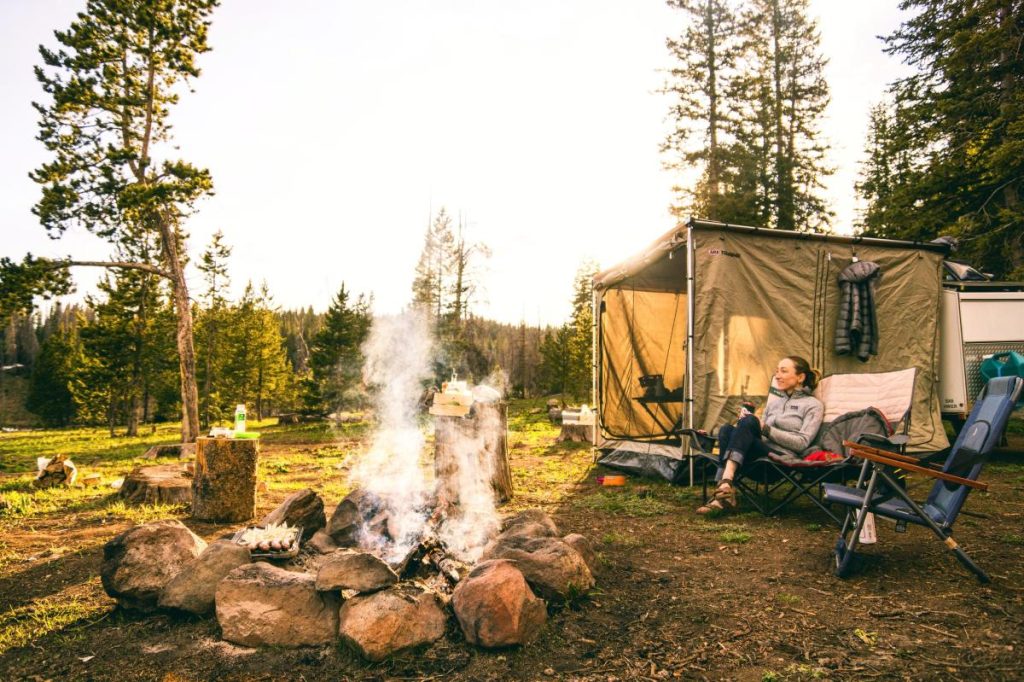 woman in camp chair near tent and campfire