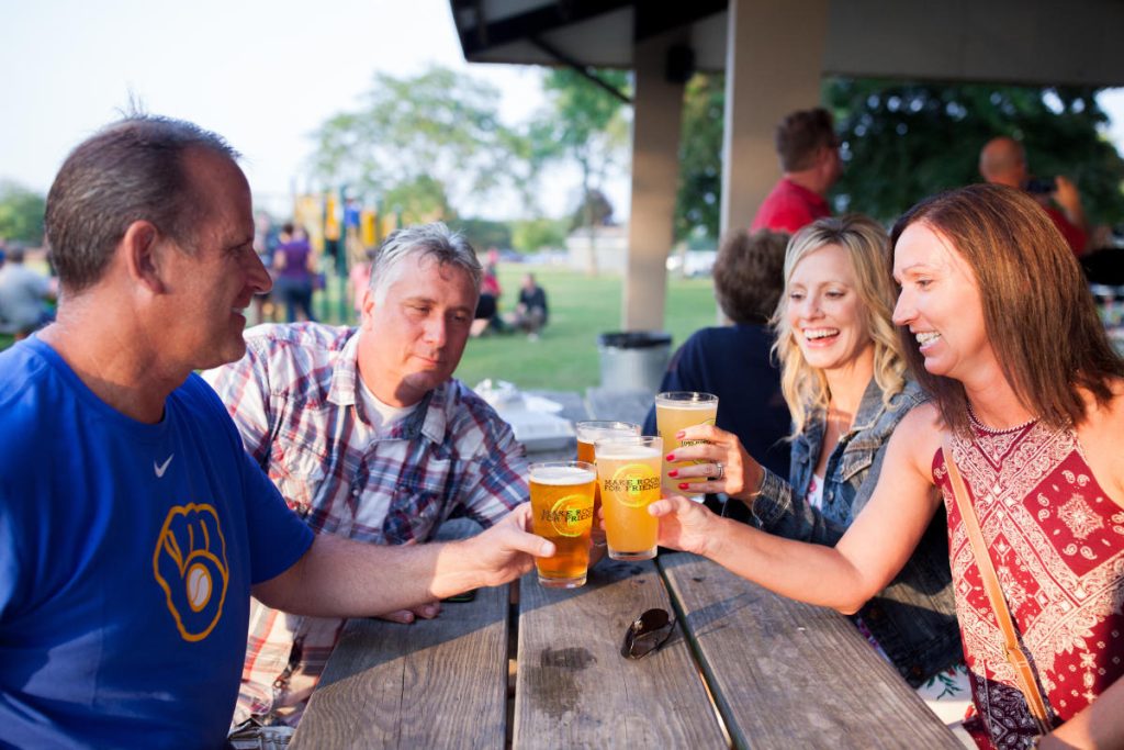 2 couples toasting with pints of beer at picnic table