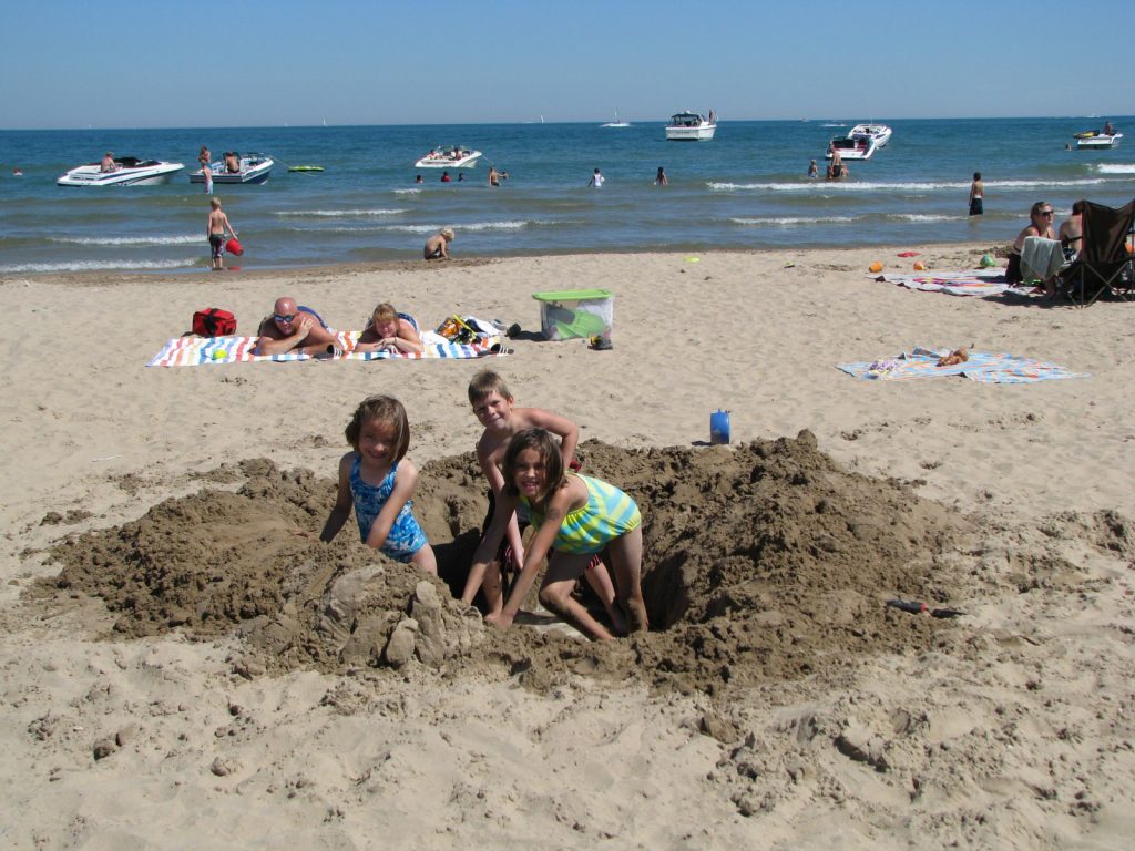 North_Beach kids digging a sand hole, sunbathers, boats on the water